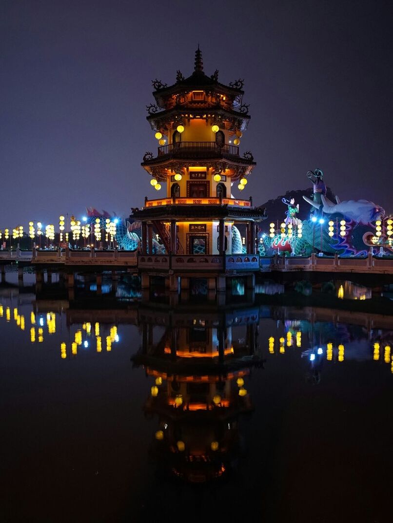 Reflection of illuminated temple in lotus lake against sky at night