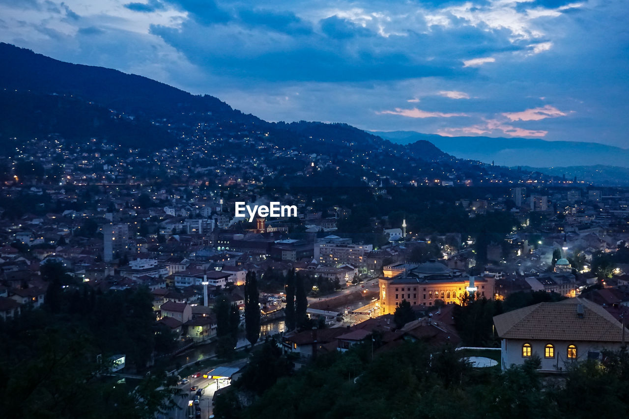 High angle view of illuminated cityscape against cloudy sky during sunset