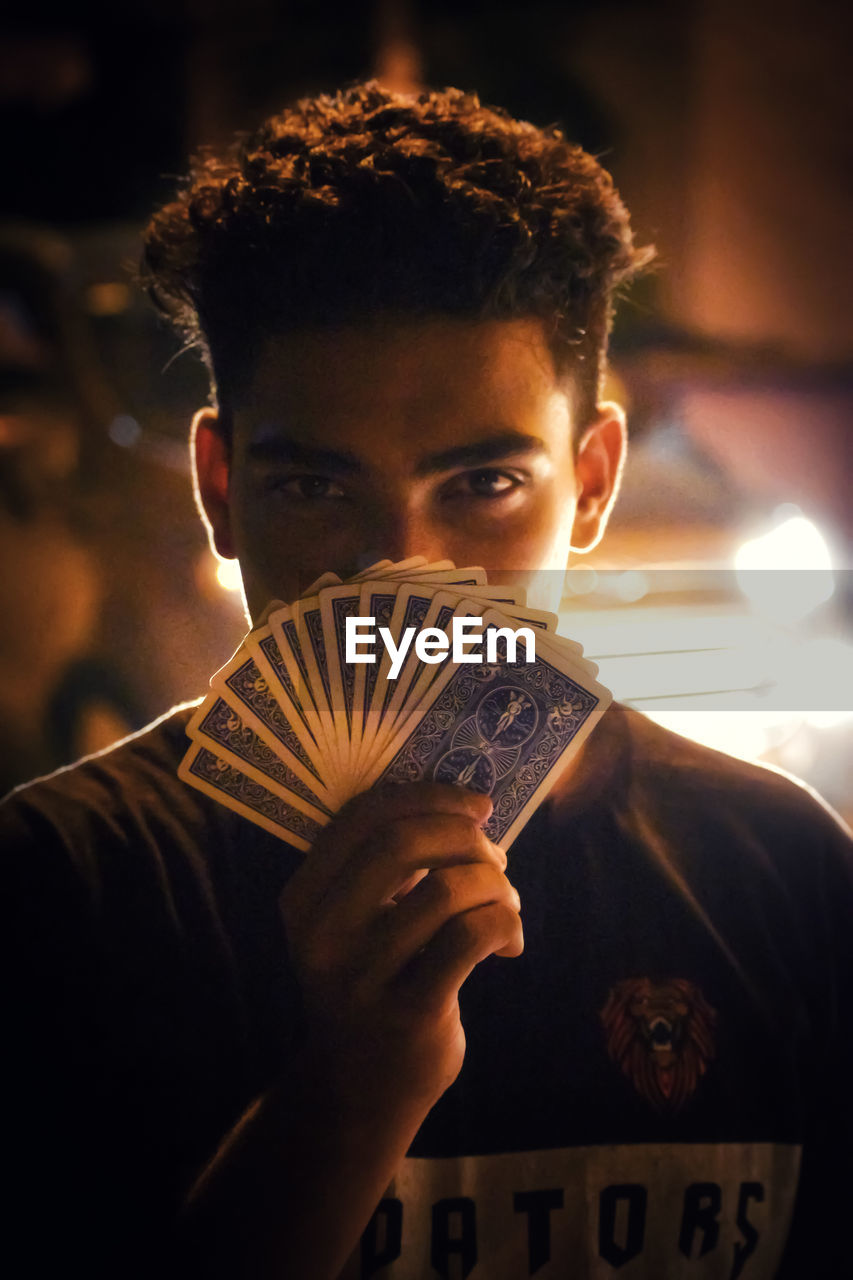 Close-up portrait of young man holding playing cards at night