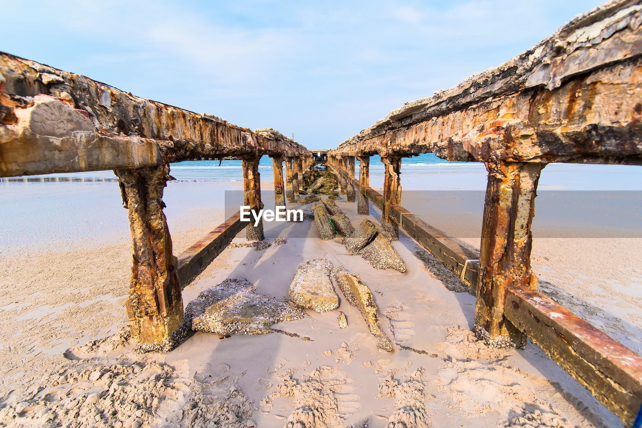 Abandoned pier on beach against sky