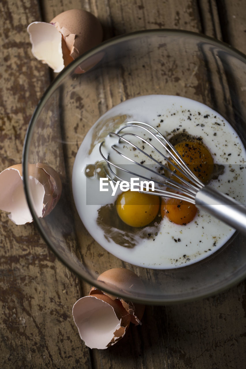 High angle view of wire whisk and eggs in bowl on table