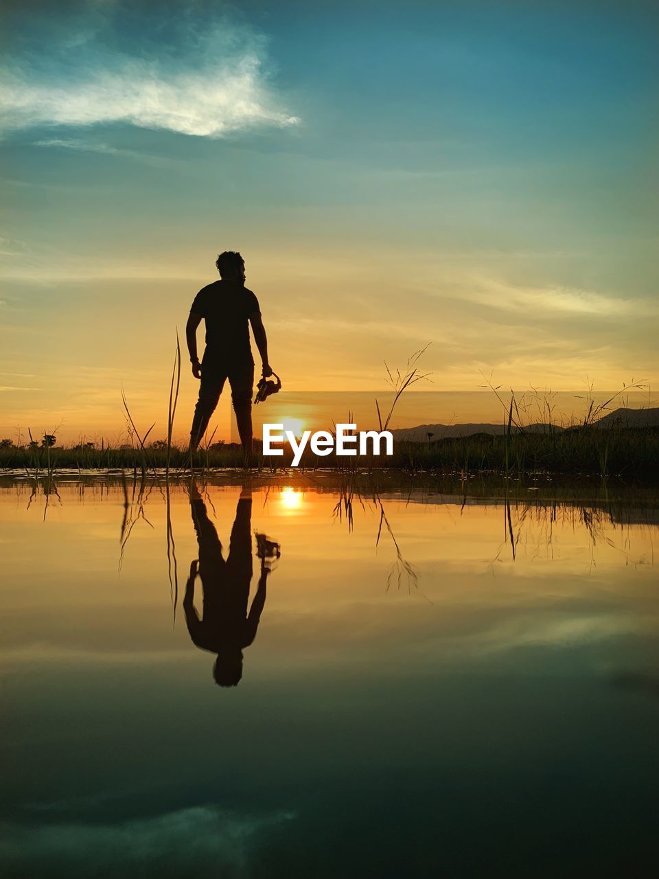Silhouette man on lake against sky during sunset