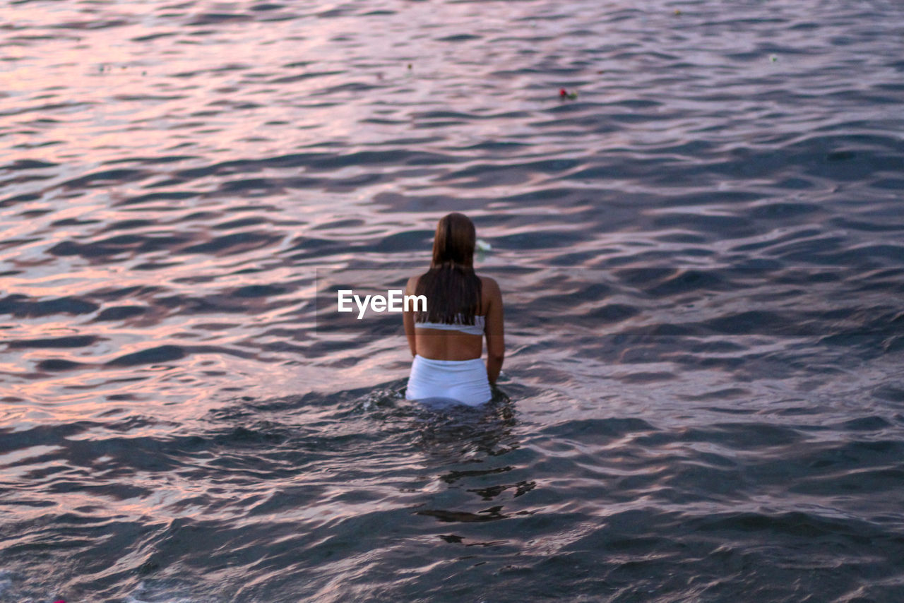 REAR VIEW OF WOMAN STANDING AT SEA SHORE