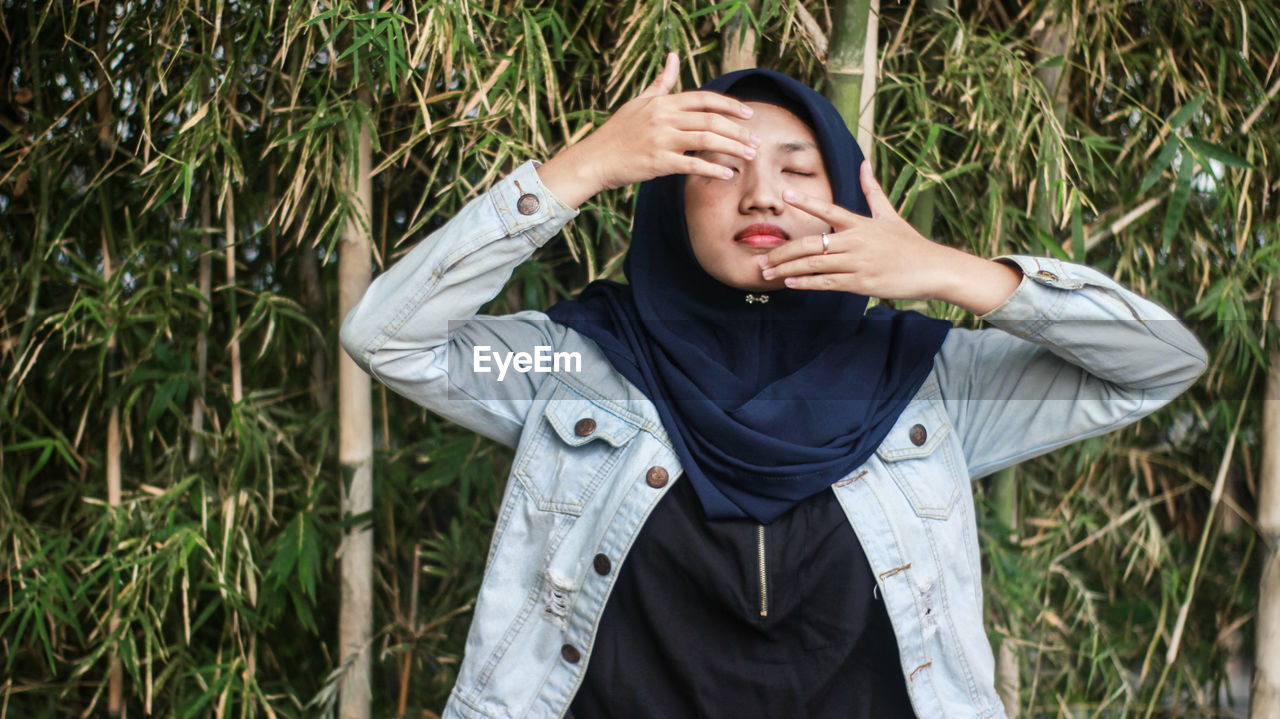 Thoughtful woman with eyes closed standing against bamboos