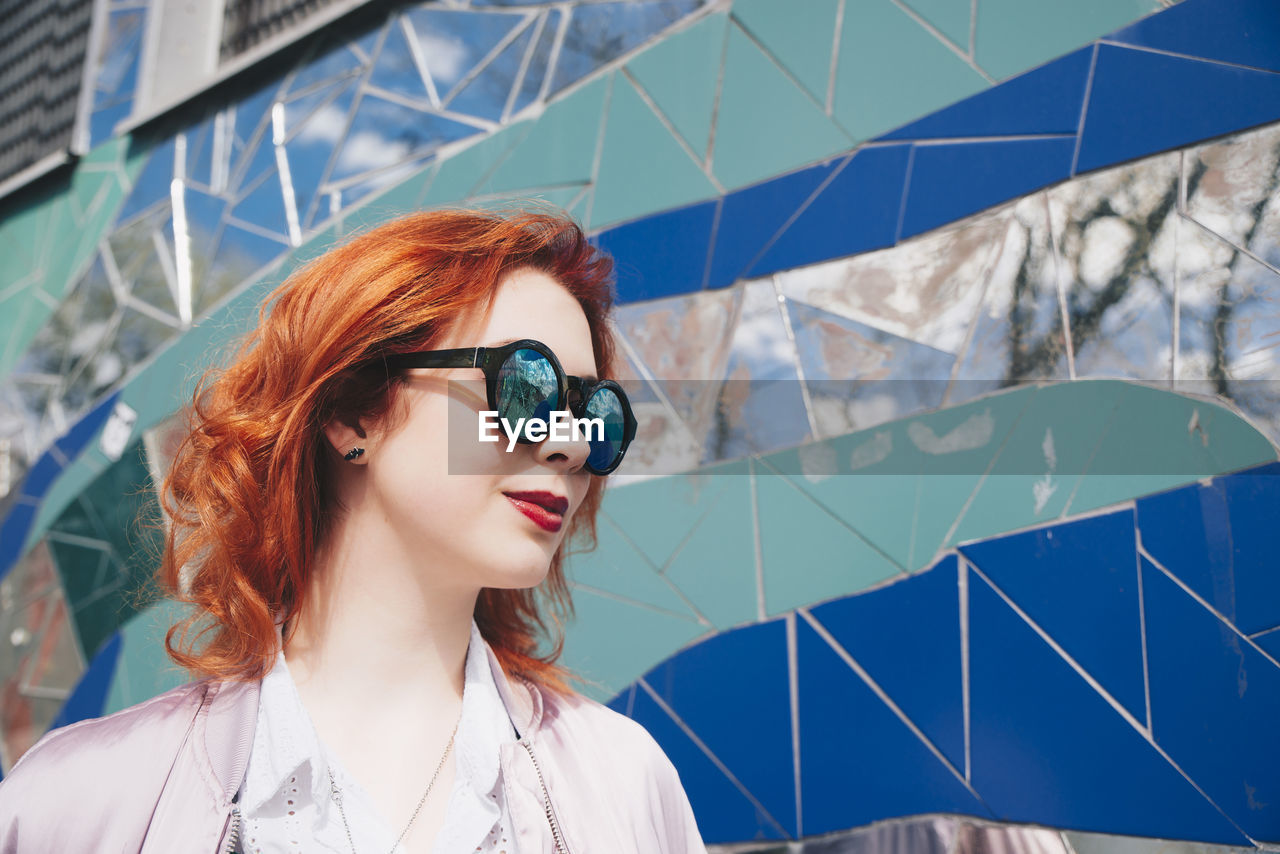 Redhead young woman wearing sunglasses against mosaic wall