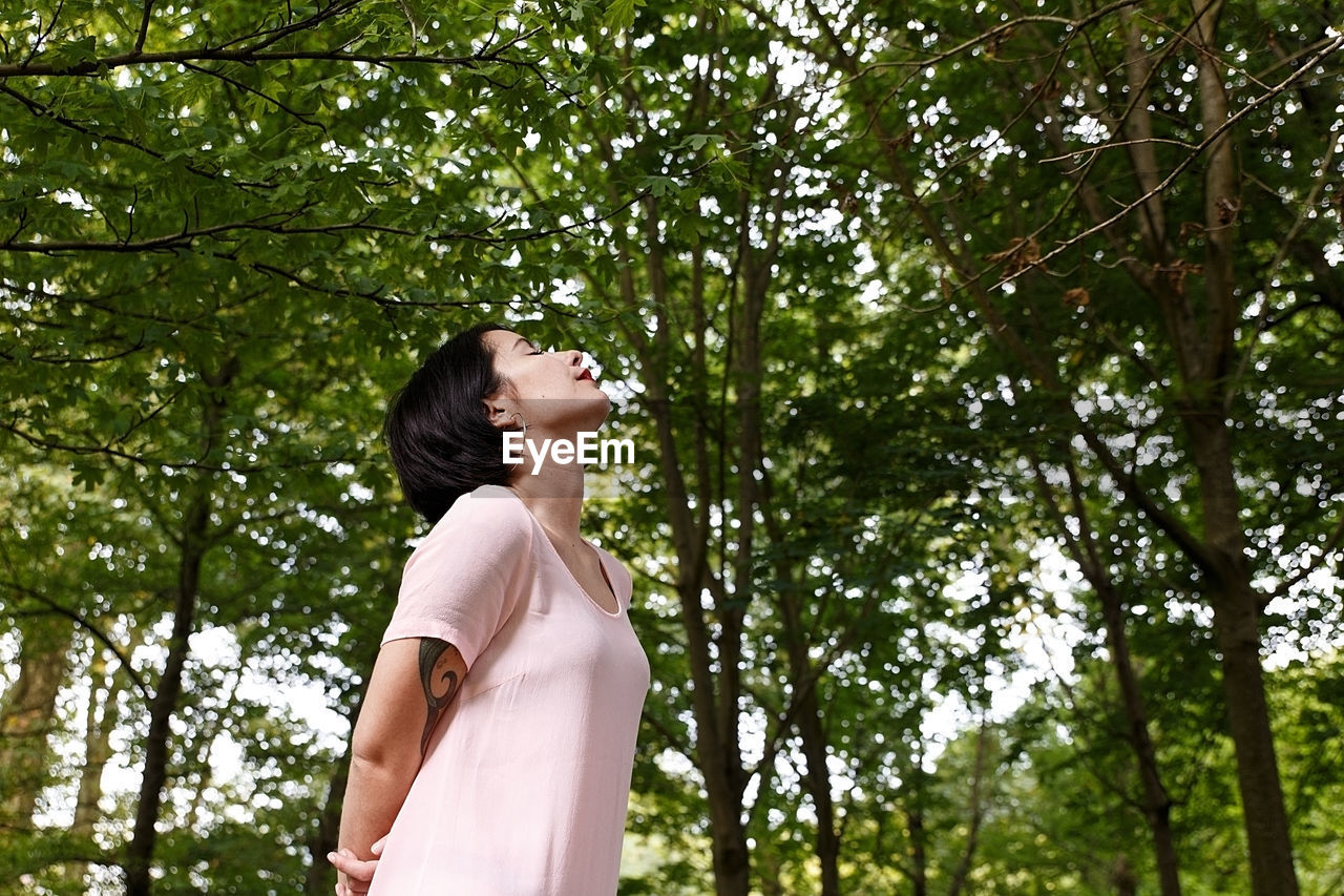 Low angle view of woman standing against trees in forest