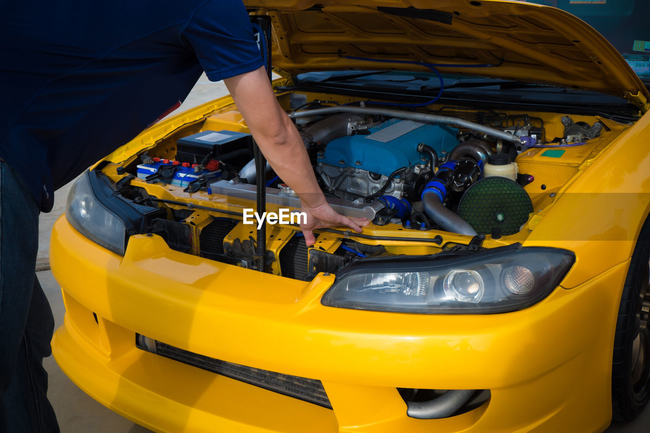 Midsection of mechanic standing by yellow car