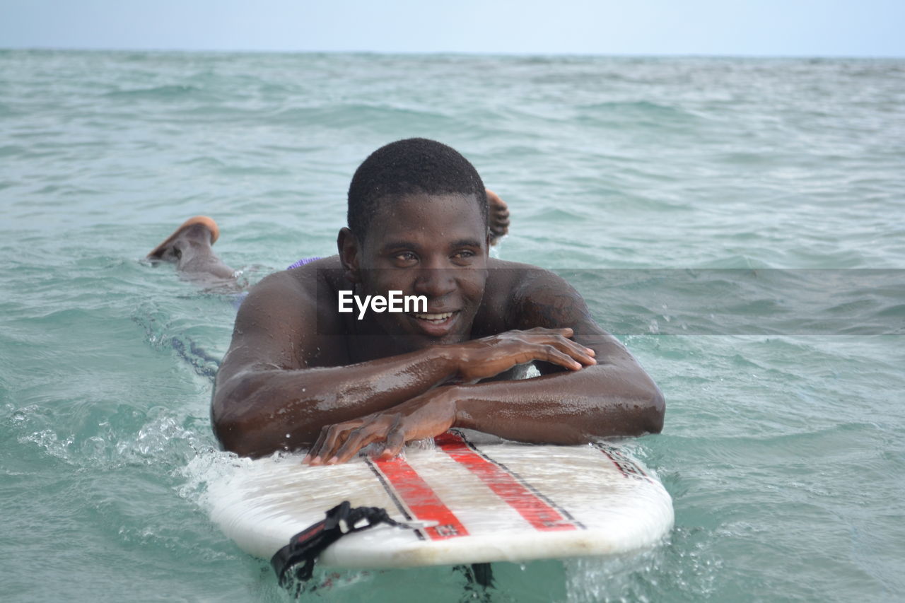 Thoughtful young man lying on surfboard in sea