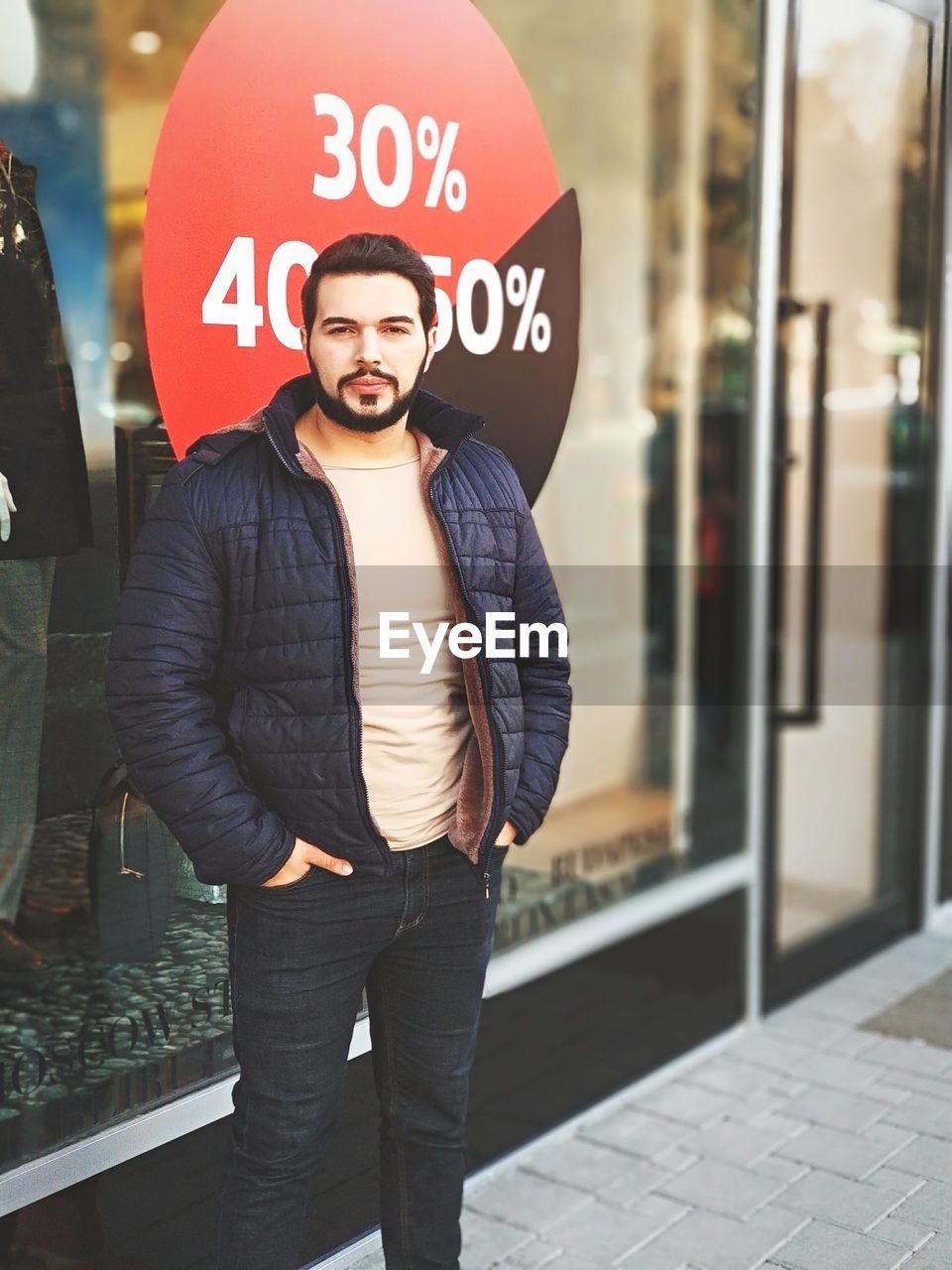 Portrait of confident man standing with hands in pockets against store