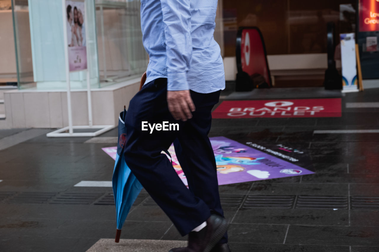 LOW SECTION OF MAN STANDING ON STREET AGAINST BUILDING