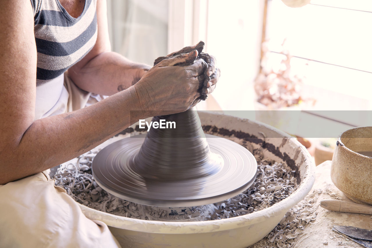 Midsection of woman making pot with clay on pottery wheel