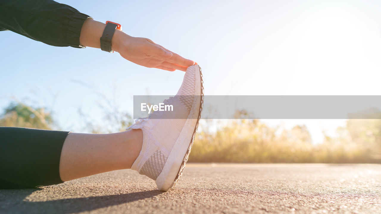 Low section of woman exercising on footpath against sky