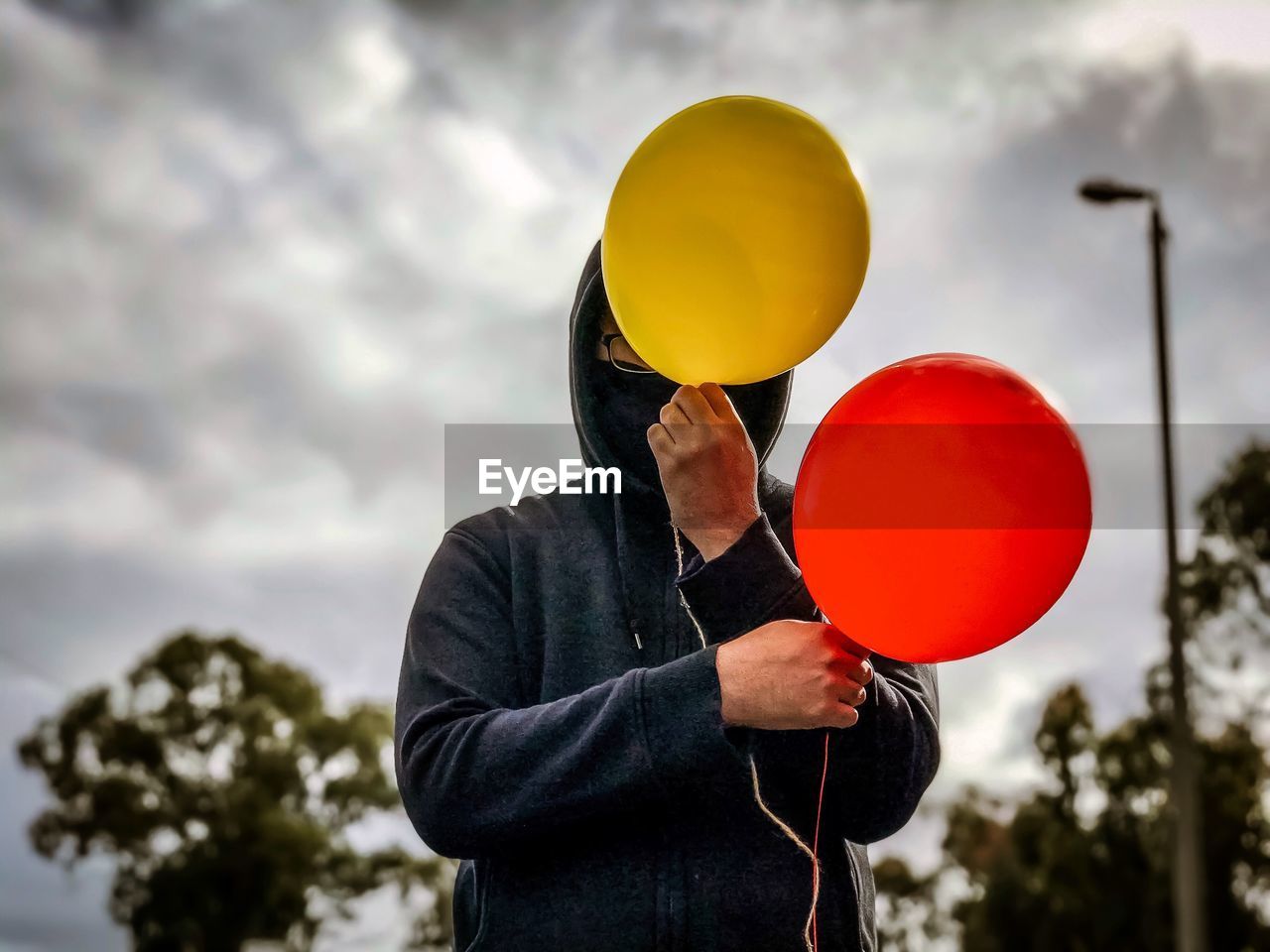 Person holding red and yellow balloons against sky.