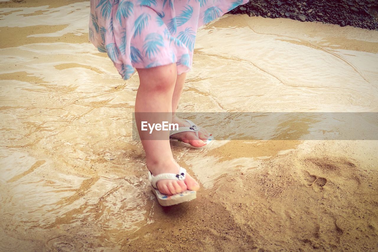 LOW SECTION OF WOMAN STANDING ON SAND