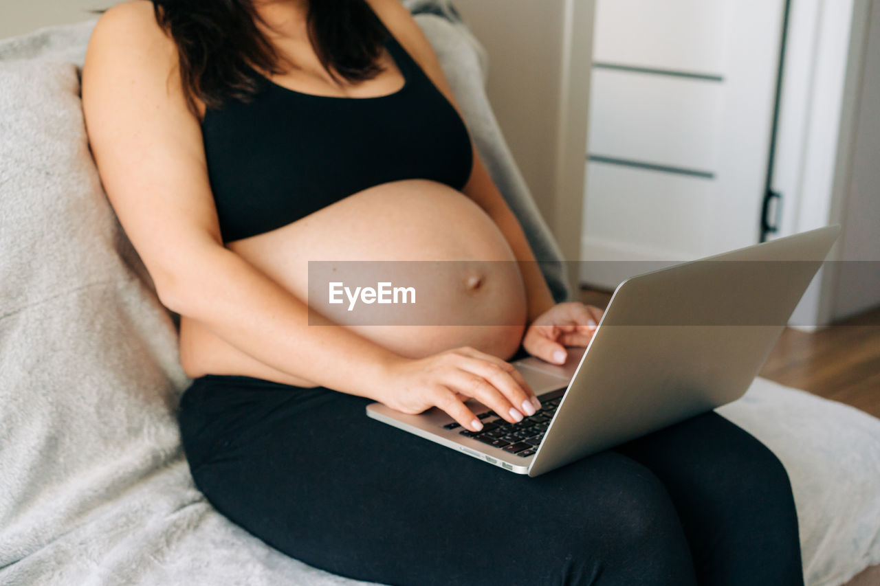 Unrecognizable pregnant business woman working at home on a laptop.