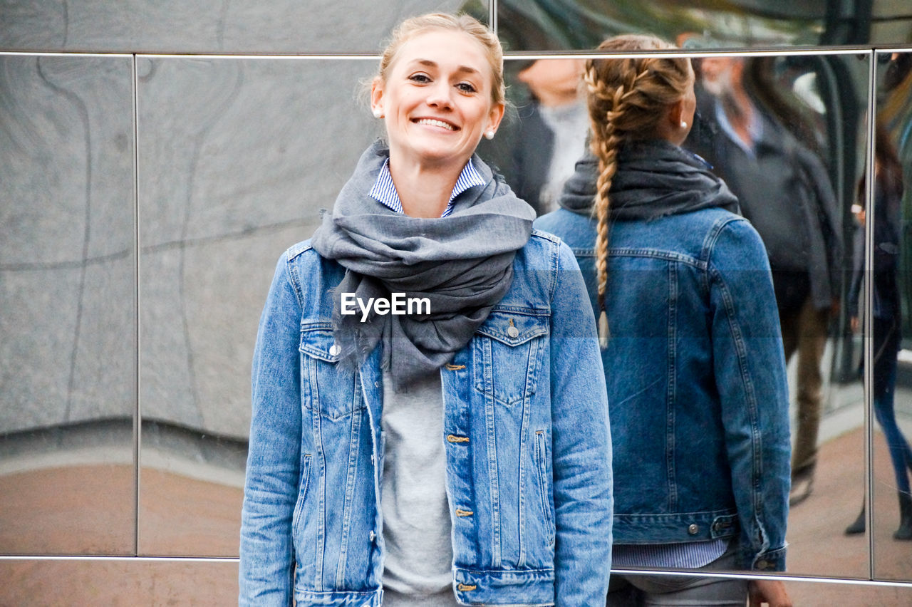 Portrait of smiling woman standing against mirror