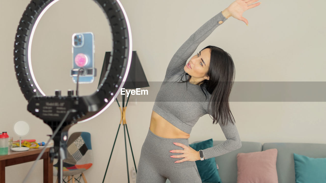 Beautiful woman exercising while vlogging at home