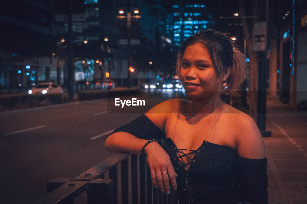 PORTRAIT OF SMILING WOMAN STANDING ON STREET AT NIGHT