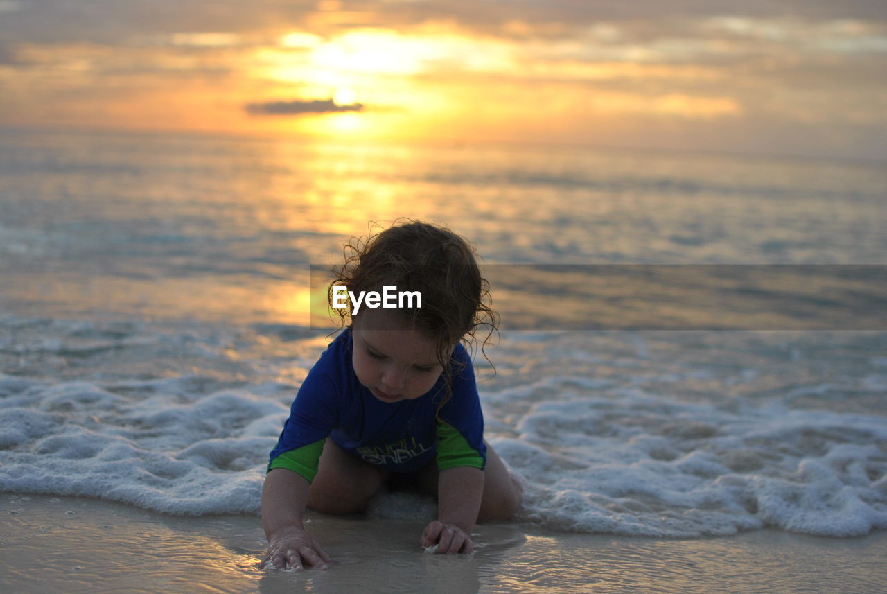 Girl playing with water at beach against sky during sunset