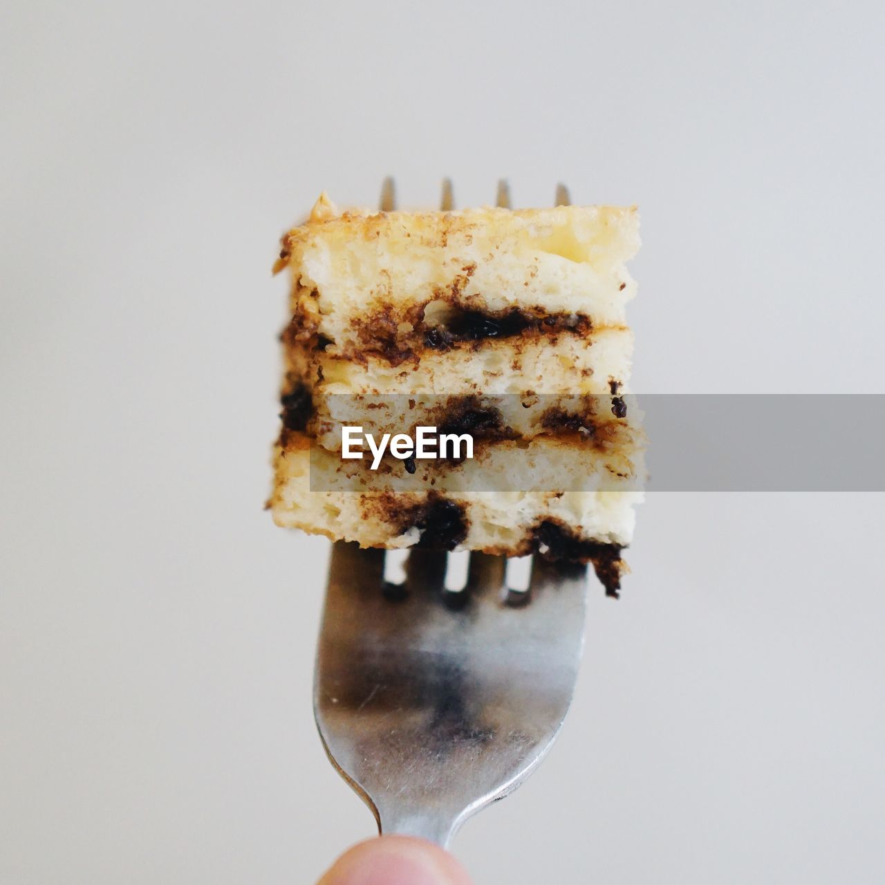Close-up of fork with cake slice over white background