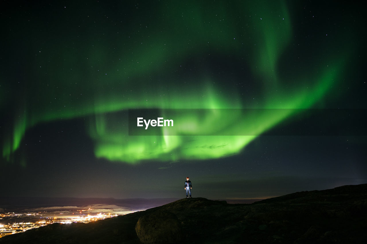 Man standing on mountain against aurora borealis