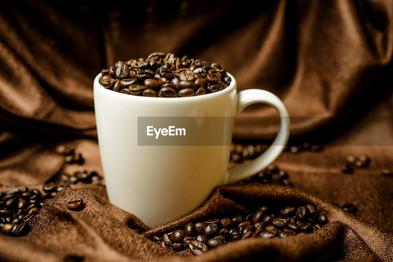 Close-up of roasted coffee beans with cup on fabric