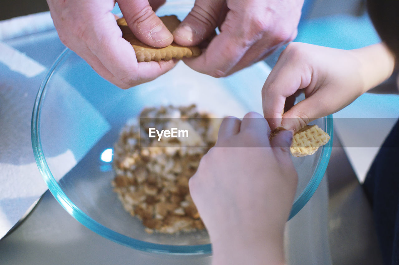 Cropped hands of father and son breaking biscuits in bowl on table