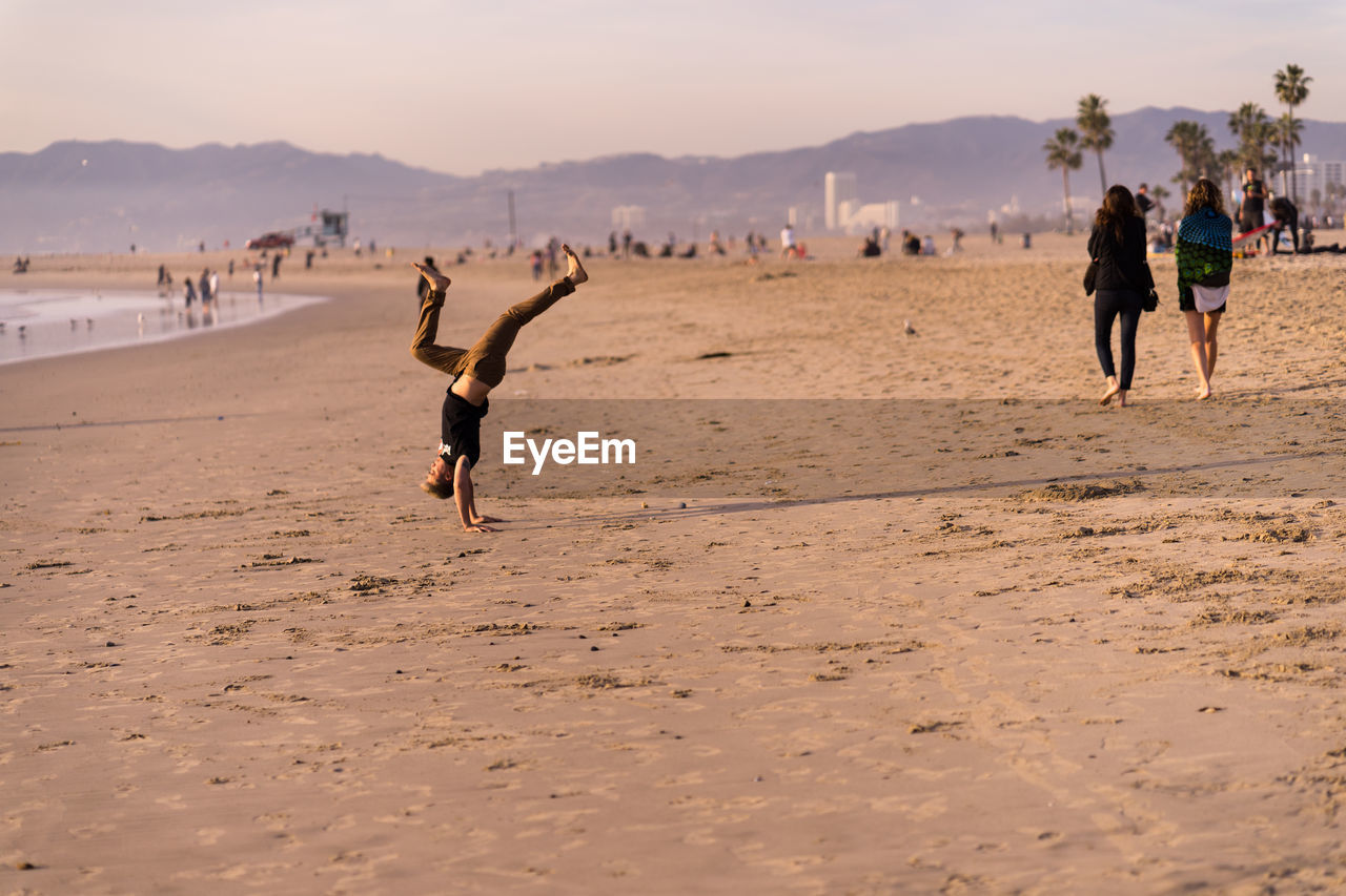 PEOPLE ENJOYING ON BEACH AGAINST SKY