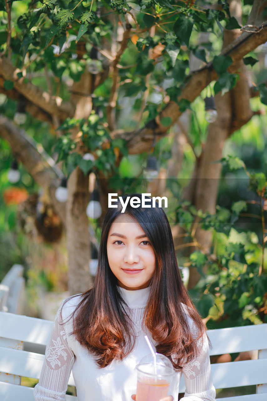 Portrait of smiling young woman against trees