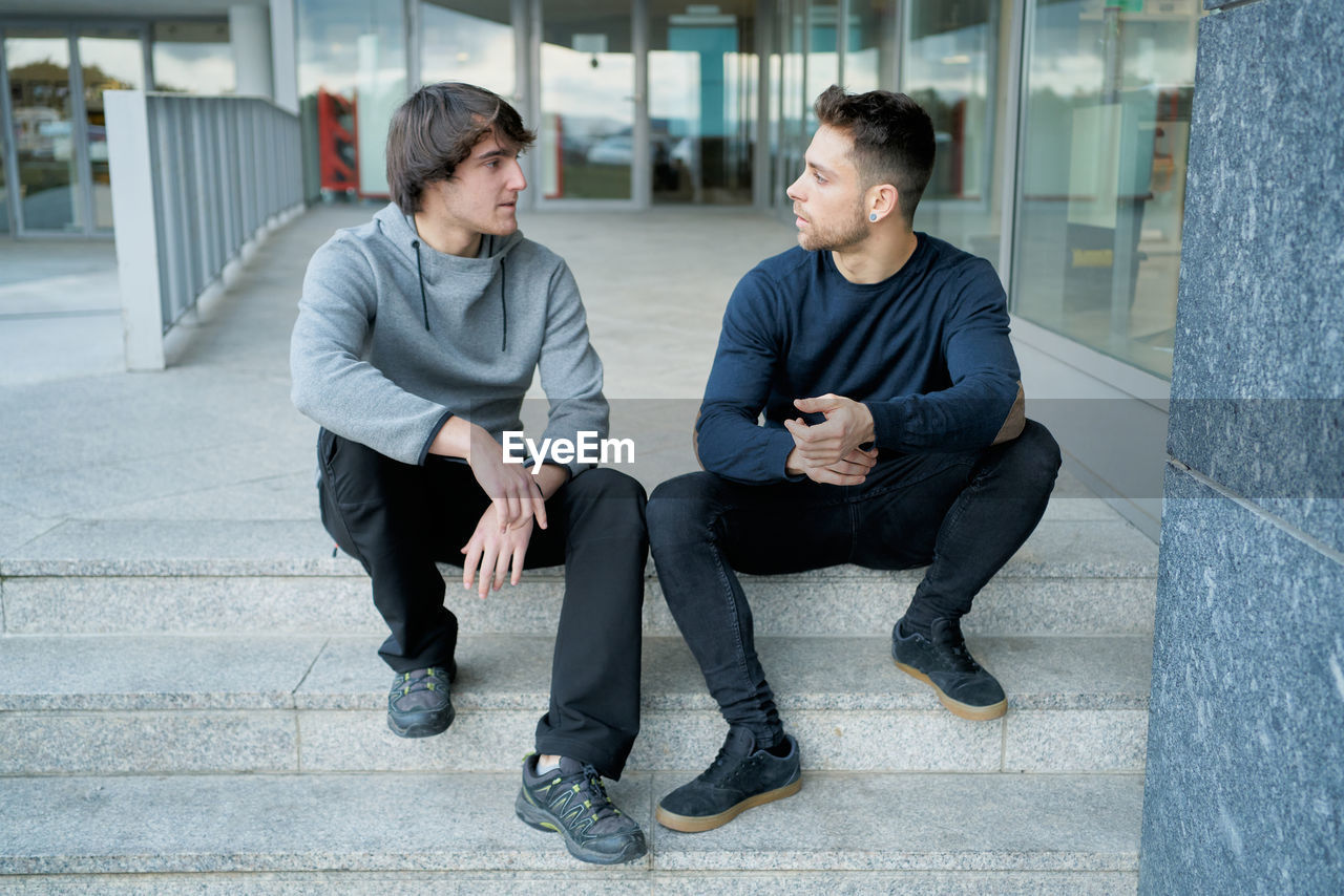 Front view of two young men talking sitting on a city staircase