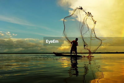 Man throwing fishing net in lake against sky