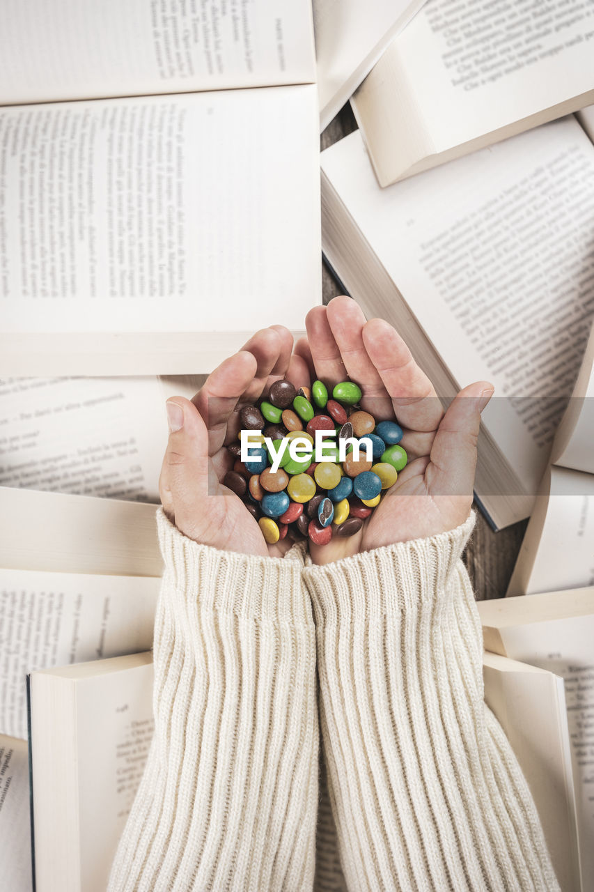Close-up of colorful round candies in hands of woman on background of open books. top view