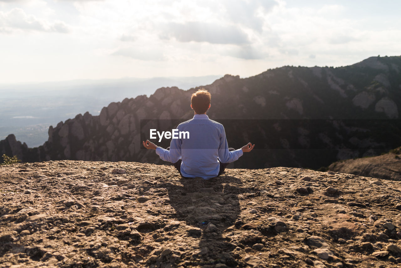 Rear view of man doing yoga on mountain against sky