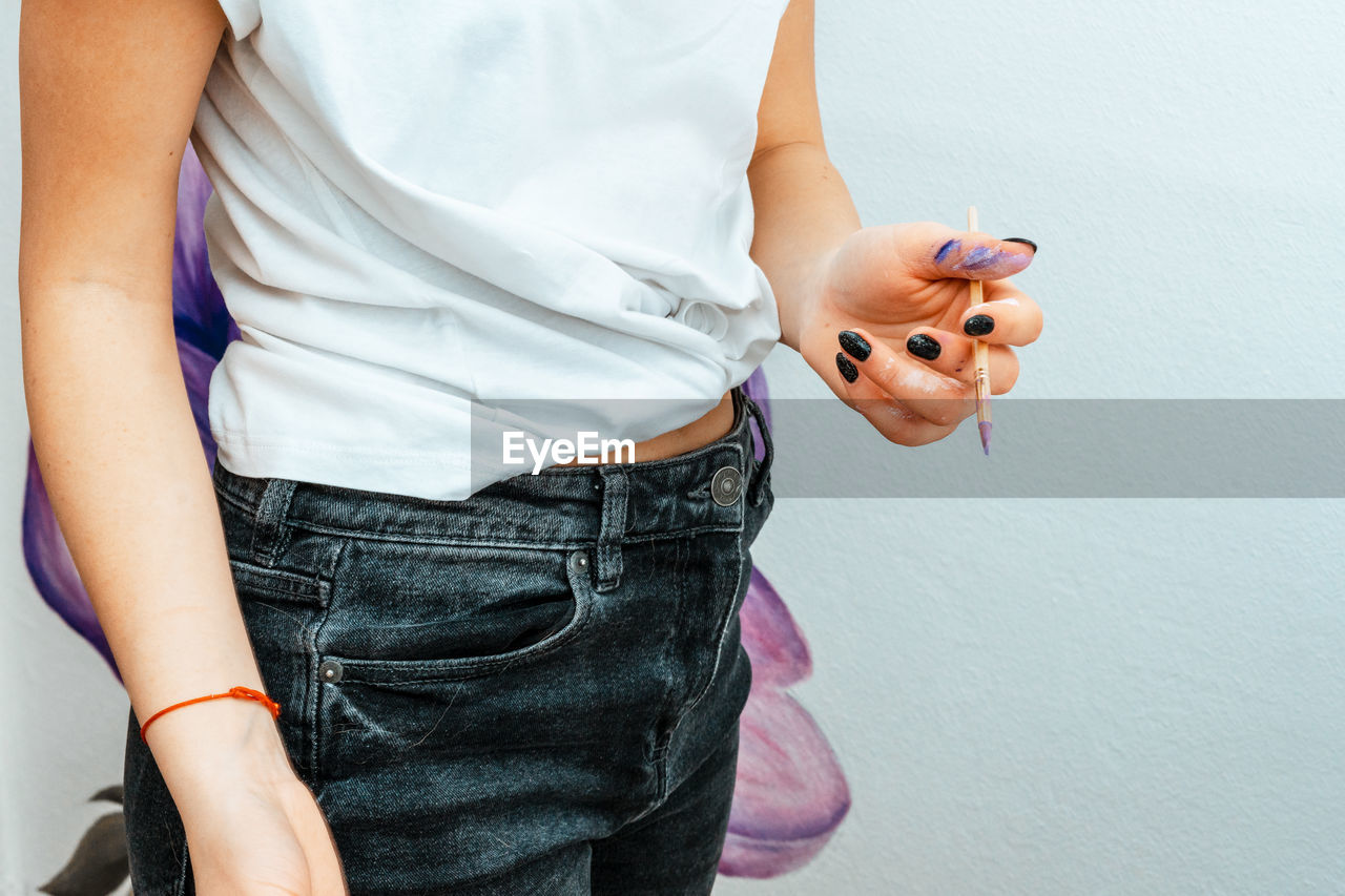 MIDSECTION OF WOMAN WEARING SUNGLASSES STANDING BY WALL