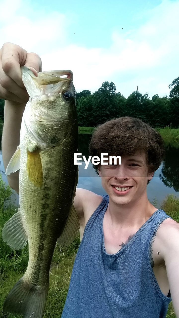 Portrait of smiling man holding caught fish at lake