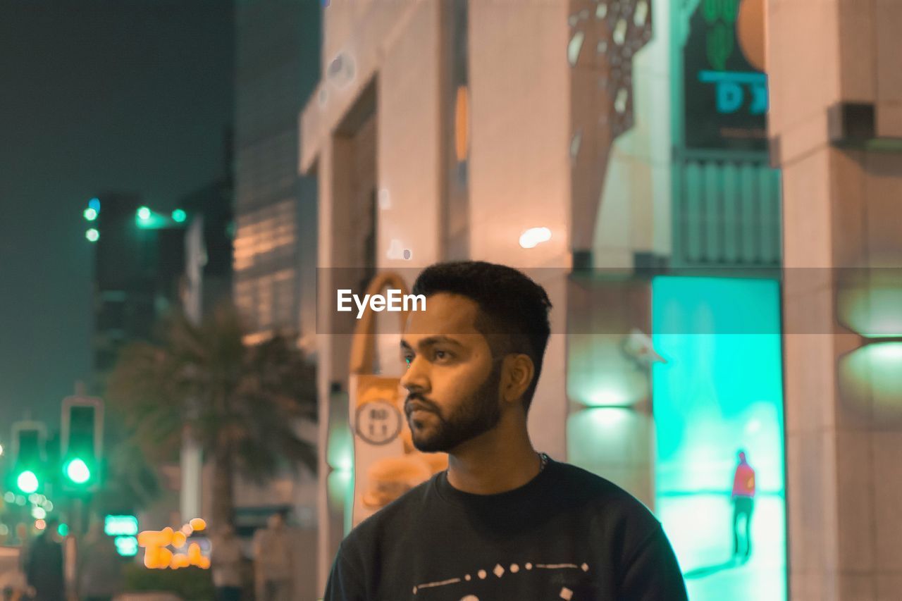 MAN LOOKING AT ILLUMINATED CITY AT NIGHT