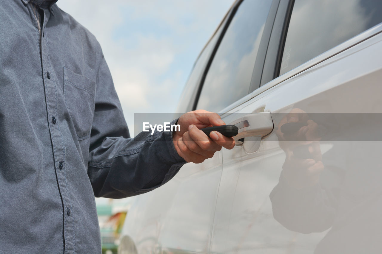 MAN HOLDING MOBILE PHONE WHILE STANDING BY CAR ON BRIDGE