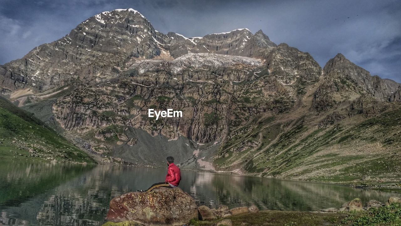 Man sitting on rock by lake against mountain