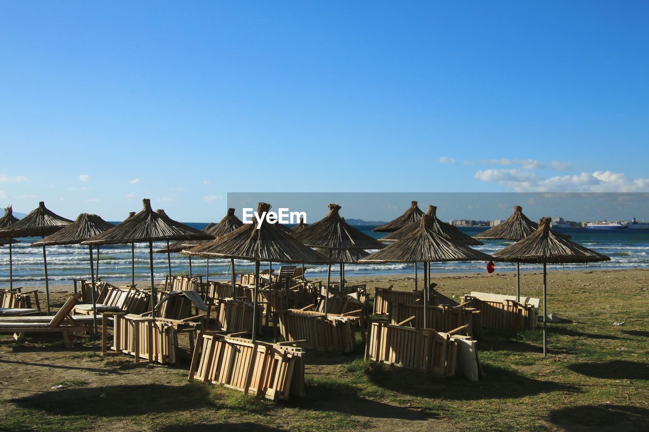 sky, water, land, nature, beach, sea, travel destinations, no people, beauty in nature, tranquility, sunlight, scenics - nature, day, travel, architecture, chair, trip, blue, holiday, sunny, vacation, sand, in a row, outdoors, clear sky, summer, tranquil scene, thatched roof, tourism, parasol, coast, body of water, idyllic, beach umbrella, horizon, copy space, sunshade, relaxation, hut, horizon over water, ocean, wood, lounge chair, built structure