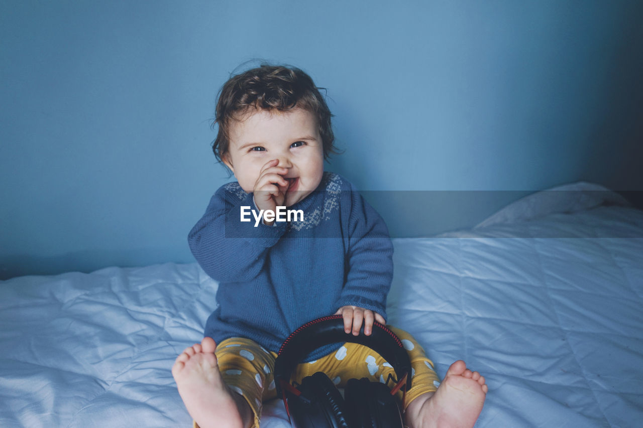 Smiling cute girl playing with headphones while sitting on bed at home