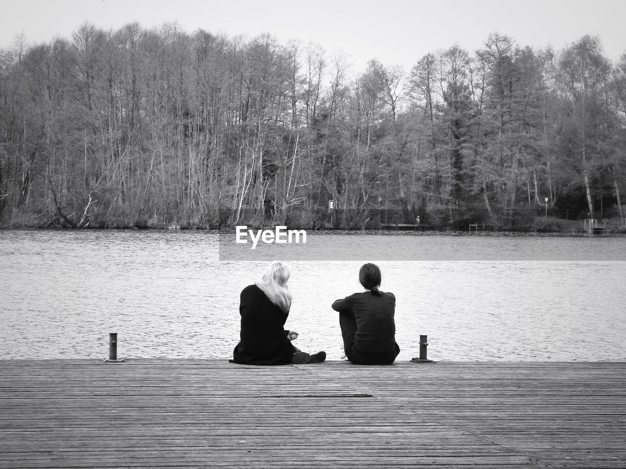 Rear view of friends relaxing on pier in front of lake