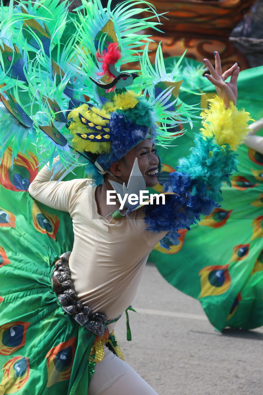 LOW ANGLE VIEW OF MAN HOLDING MULTI COLORED FEATHERS IN STREET