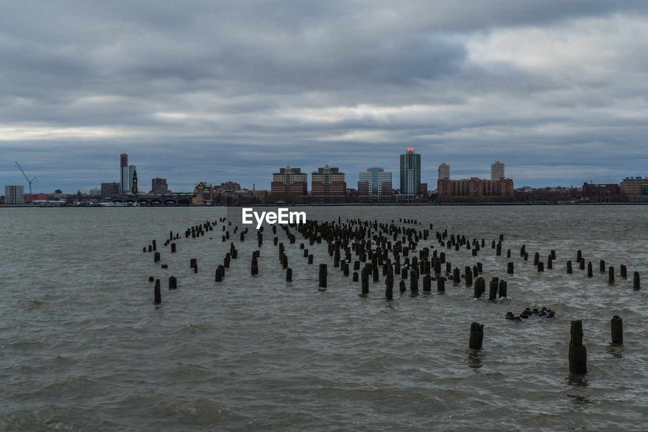 Wooden posts in sea against buildings in city