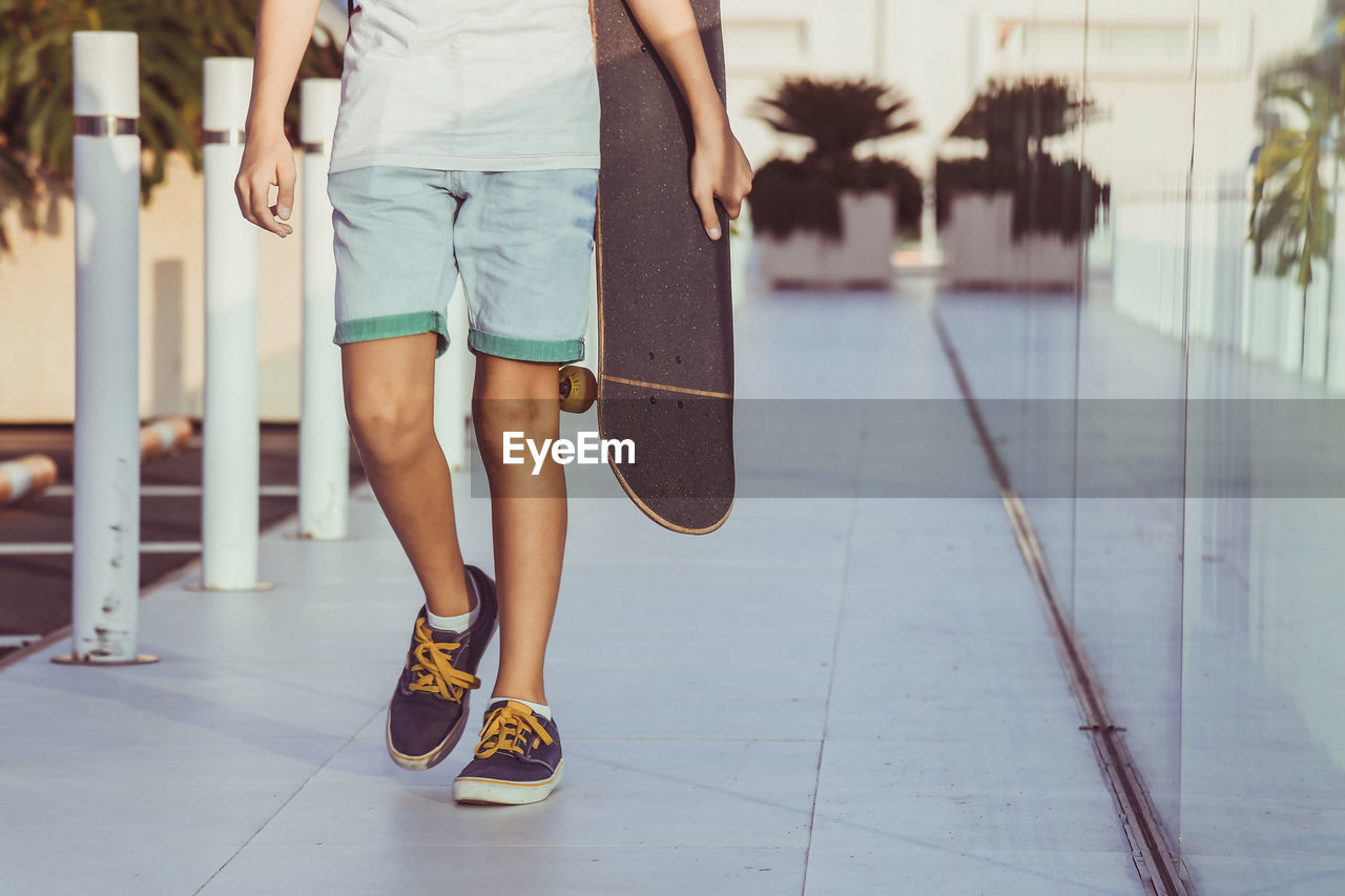 Low section of boy walking with skateboard on floor