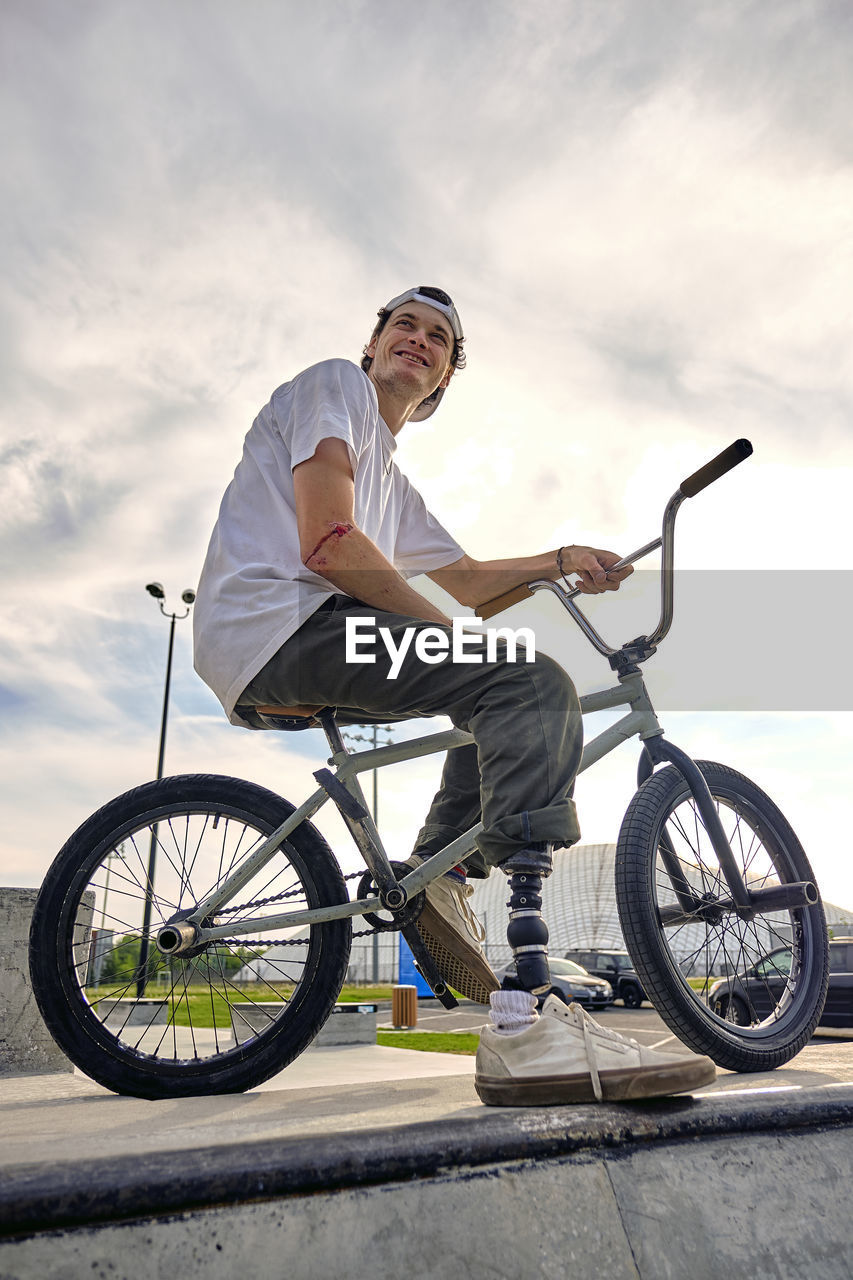 Bmx rider with prosthetic foot confidently posing on bike against cloudy sky at skateboard park