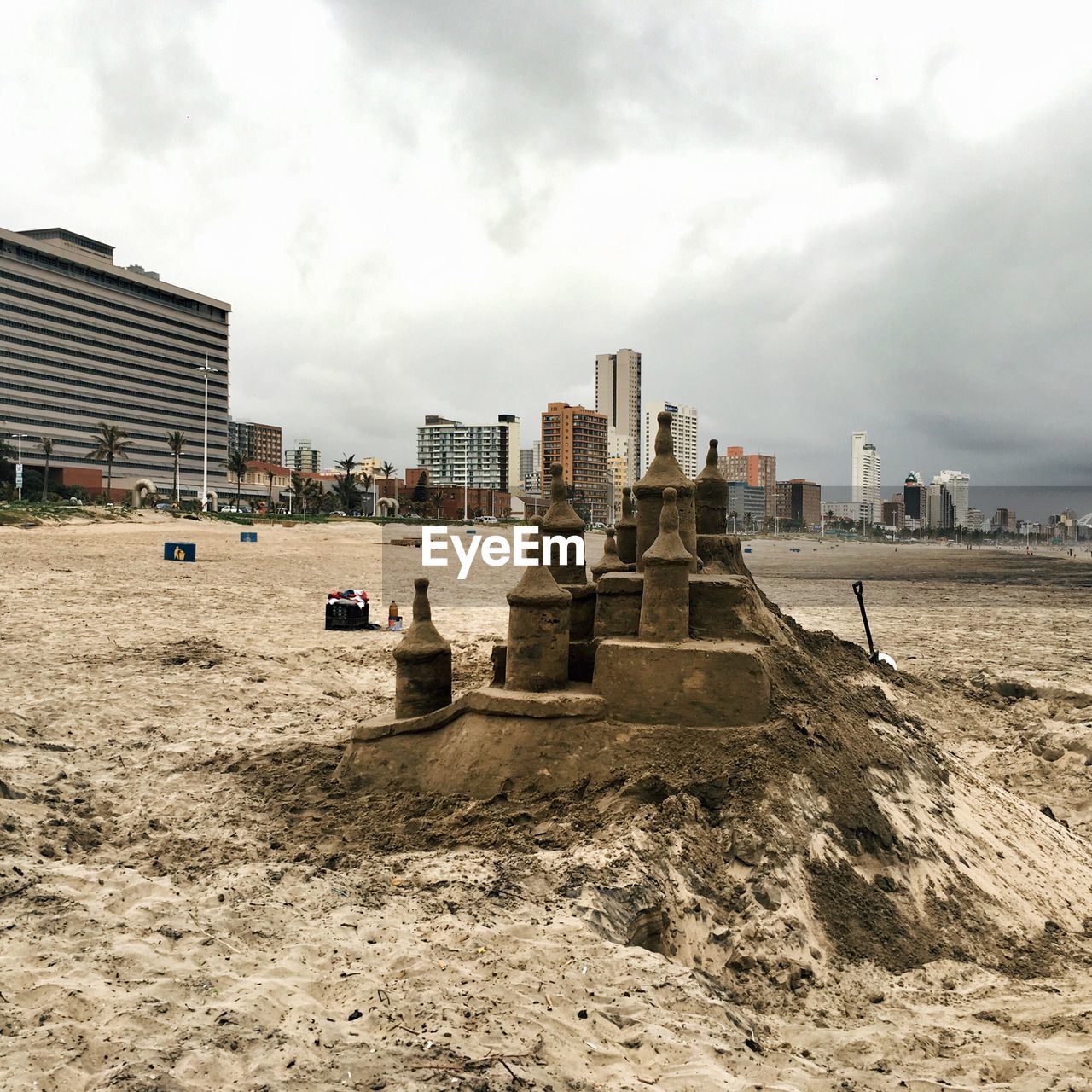 Sand castle on beach by buildings against cloudy sky