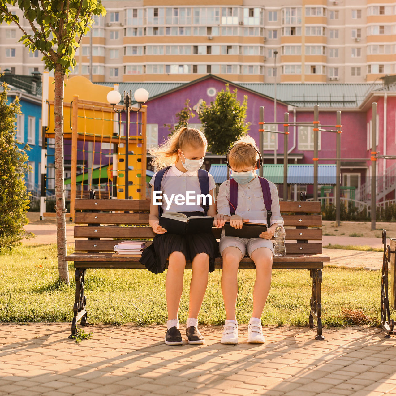 FULL LENGTH OF WOMAN SITTING ON BENCH AGAINST BUILDING