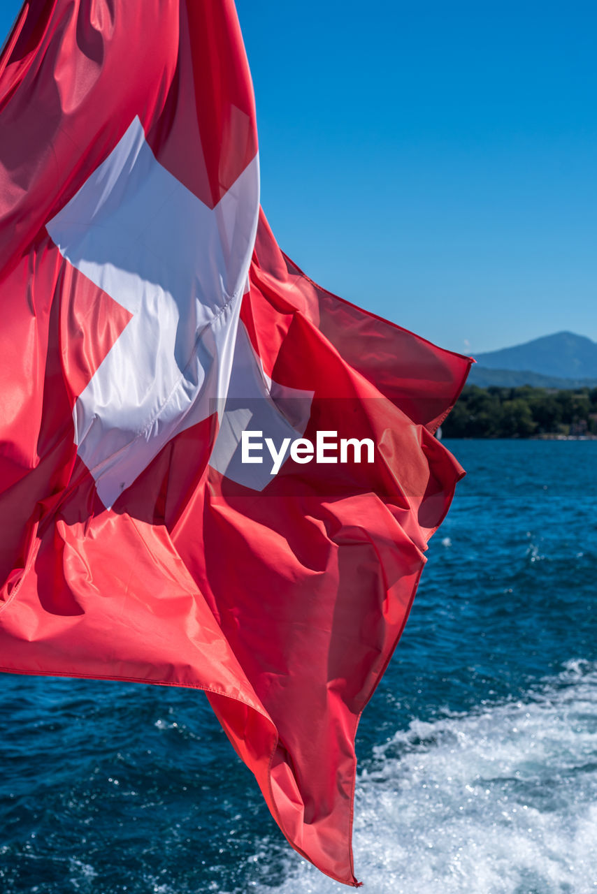 Vertical photo of the swiss flag fluttering in the wind from a boat in the wake of lake geneva.