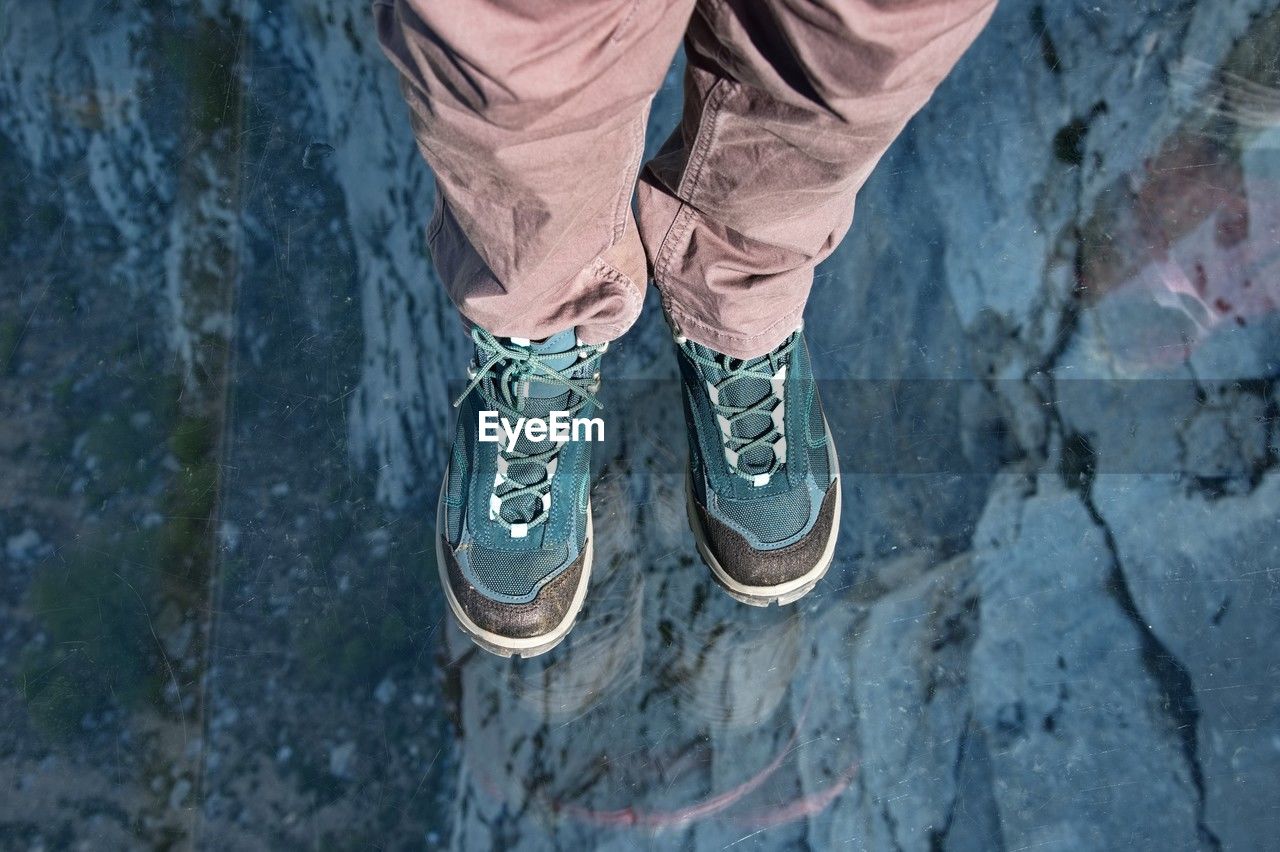 shoe, low section, human leg, one person, blue, standing, lifestyles, high angle view, day, footwear, leisure activity, spring, limb, human limb, casual clothing, men, outdoors, nature, adult, winter, rock, water, personal perspective, clothing, walking shoe, jeans, human foot, sports shoe, adventure, directly above