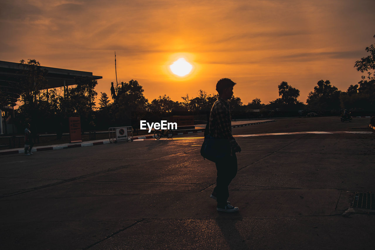 Young man standing on road during sunset